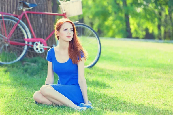 Redhead girl in blue dress with red bicycle in the park. — Stock Photo, Image