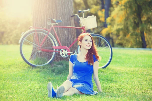 Roodharige meisje in blauwe jurk met rode fiets in het park. — Stockfoto