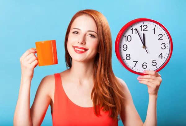 Redhead girl with tea cup and huge clock on blue background. Royalty Free Stock Photos