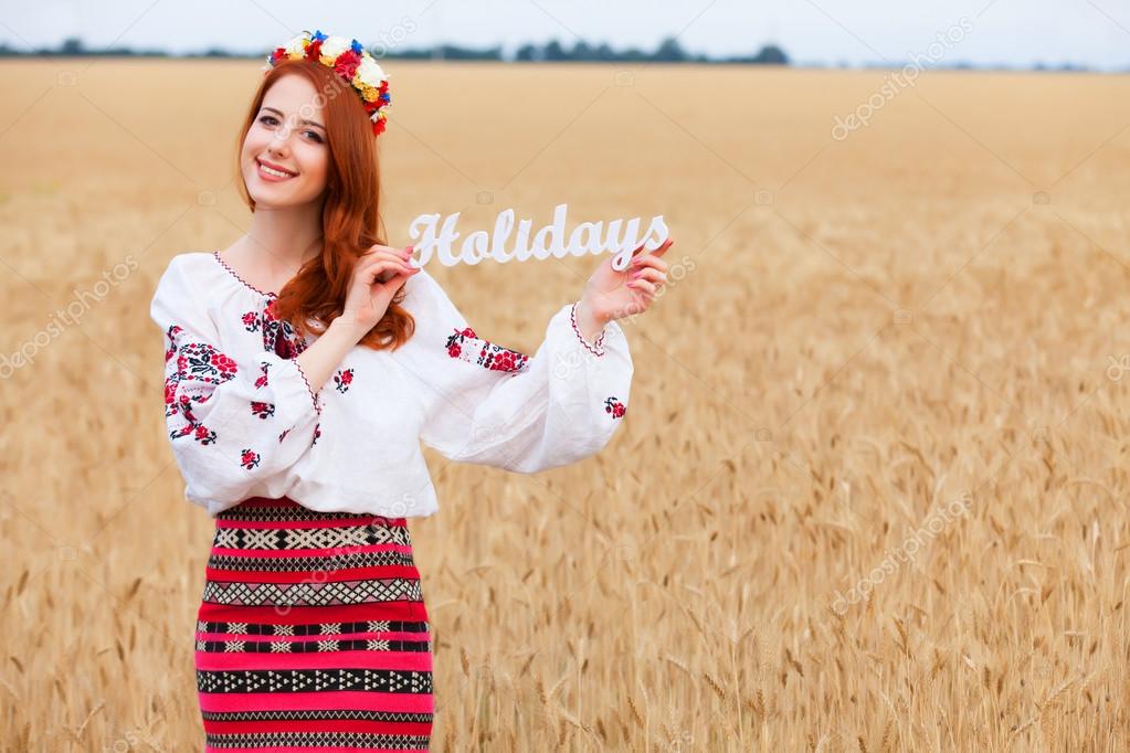 Redhead girl in national ukrainian clothes with wooden word Holi