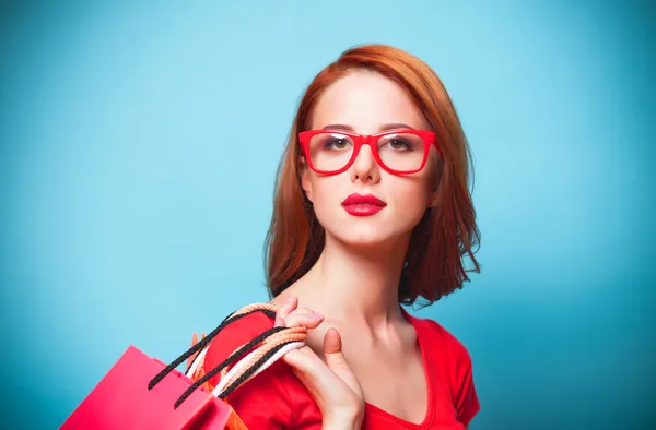 Pelirroja chica con bolsas de compras sobre fondo azul . — Foto de Stock