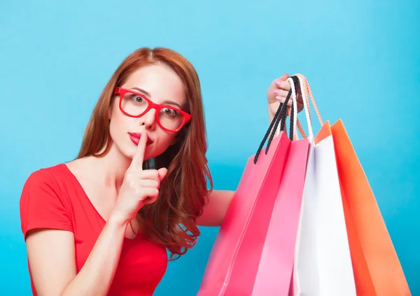 Redhead girl with shopping bags on blue background. — Stock Photo, Image