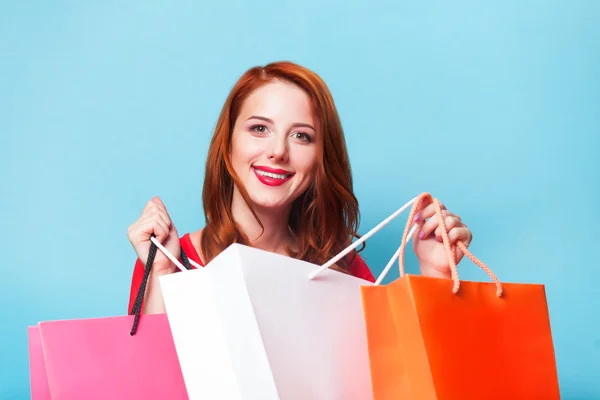 Redhead girl with shopping bags on blue background. — Stock Photo, Image