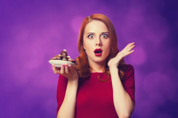 Redhead women with candy on violet background. — Stock Photo, Image