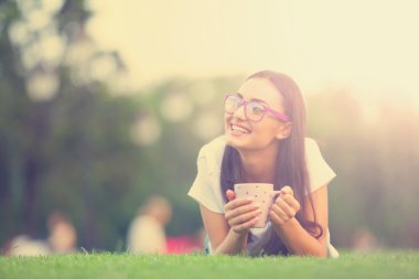 esmer kız parkta yeşil çimenlerin üzerinde kahve ile.