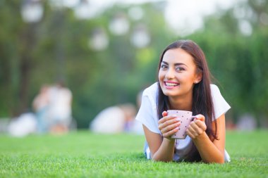 esmer kız parkta yeşil çimenlerin üzerinde kahve ile.
