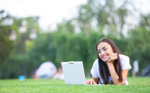 Menina morena com notebook na grama verde no parque . — Fotografia de Stock