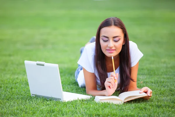 Chica morena con cuaderno y libro sobre hierba verde en el parque . —  Fotos de Stock