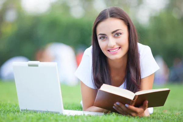 Brunette meisje met notebook en boek over groen gras in het park. — Stockfoto