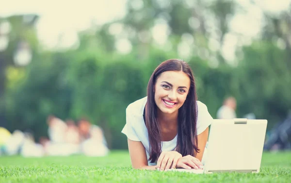 Brunetka dziewczynka z notebooka na zielonej trawie w parku. — Zdjęcie stockowe