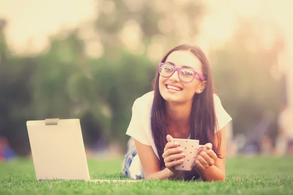 Roodharige meisje met notebook en kopje koffie op het groene gras. — Stockfoto