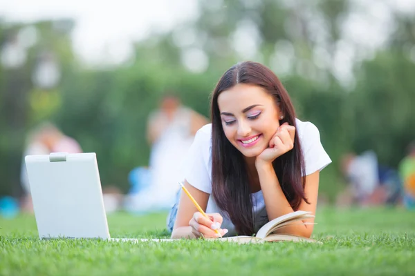 Брюнетка дівчина з блокнот і книгу на зелені травичці в парку. — стокове фото