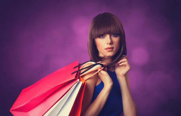 Brunette meisje met boodschappentassen op violette achtergrond. — Stockfoto