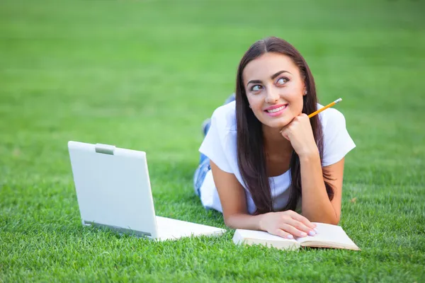 Chica morena con cuaderno y libro sobre hierba verde en el parque . — Foto de Stock