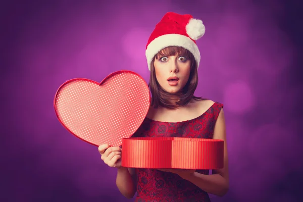 Mädchen mit Weihnachtsmütze mit Geschenkschachtel auf violettem Hintergrund. — Stockfoto