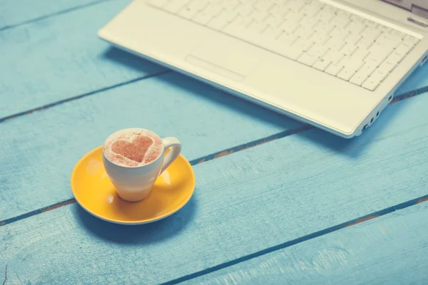 Fincan kahve ve mavi ahşap masa üstünde laptop. — Stok fotoğraf