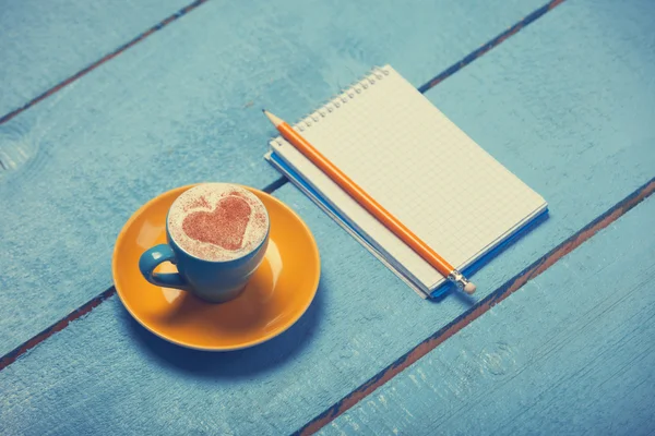 Xícara de café com forma de coração e lápis com notebook — Fotografia de Stock