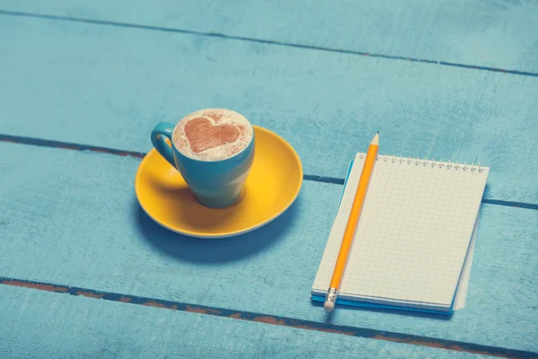 Taza de café con forma de corazón y lápiz con cuaderno — Foto de Stock
