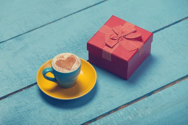 Cup of coffee with heart shape and gift on blue wooden table. — Stock Photo, Image