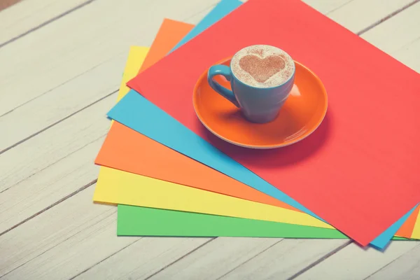 Kopp kaffe och färg papper på träbord. — Stockfoto