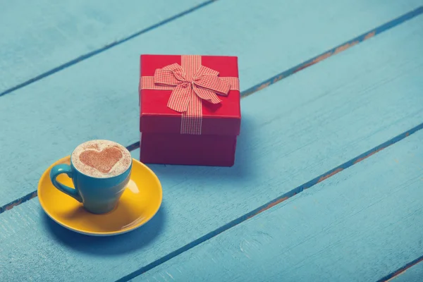 Kopp kaffe med hjärta form och gåva på blå träbord. — Stockfoto