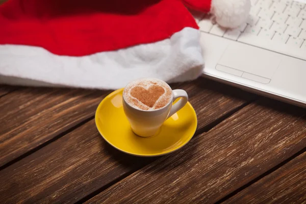 Cup of coffee with heart shape, laptop and christmas hat. — Stock Photo, Image