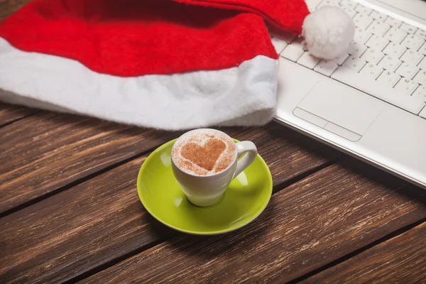 Cup of coffee with heart shape, laptop and christmas hat. — Stock Photo, Image
