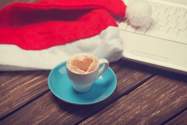 Cup of coffee with heart shape, laptop and christmas hat. — Stock Photo, Image