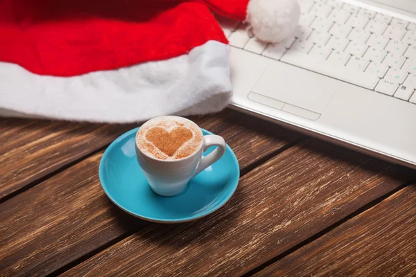 Kopp kaffe med hjärta form, laptop och jul hatt. — Stockfoto