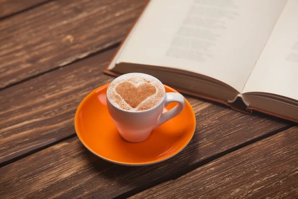 Kopp kaffe med hjärta form och bok om träbord. — Stockfoto