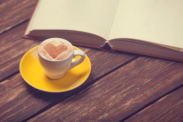 Xícara de café com forma de coração e livro em mesa de madeira . — Fotografia de Stock