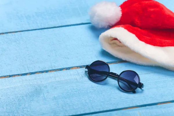 Sonnenbrille und Weihnachtsmütze auf blauem Holz — Stockfoto