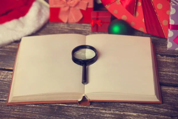 Büyüteç ve Noel hediyeleri arka plan üzerinde kitap — Stok fotoğraf
