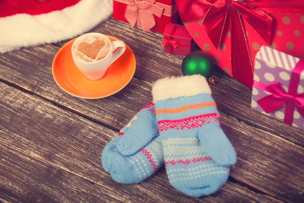 Cup of coffee with heart shape, mittens and christmas gifts. — Stock Photo, Image