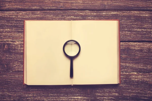 Opened book and loupe on a table. — Stock Photo, Image