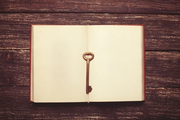 Retro key and opened book on wooden table. — Stock Photo, Image