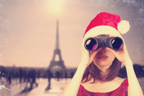 Mädchen mit Fernglas und Weihnachtsmütze und Pariser Hintergrund. — Stockfoto