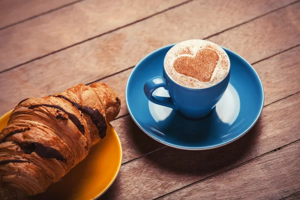 Croissant francês e xícara de café em uma mesa de madeira — Fotografia de Stock
