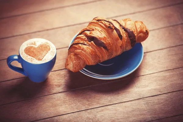 Croissant francés y taza de café en una mesa de madera — Foto de Stock