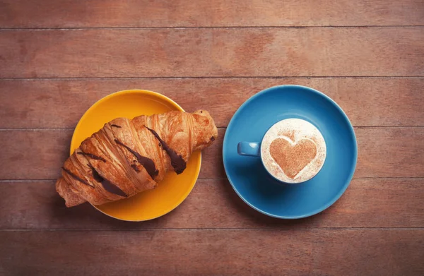 Croissant francés y taza de café en una mesa de madera — Foto de Stock