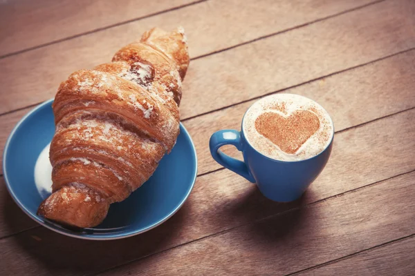 Croissant francés y taza de café en una mesa de madera — Foto de Stock