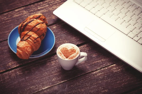 Croissant és kávét laptop a fából készült asztal. — Stock Fotó