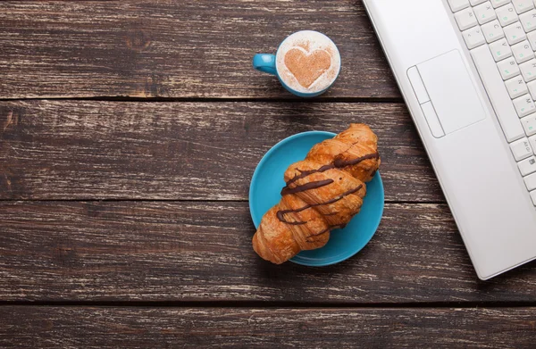 Croissant és kávét laptop a fából készült asztal. — Stock Fotó