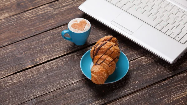 Kruvasan ve kahve ile ahşap masa üstünde laptop. — Stok fotoğraf