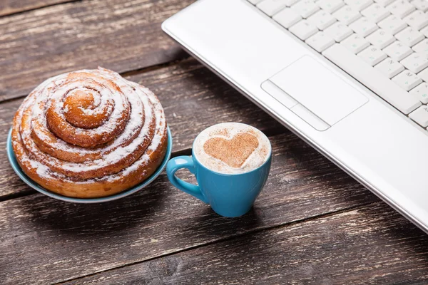 Bun och kopp kaffe med laptop på träbord. — Stockfoto