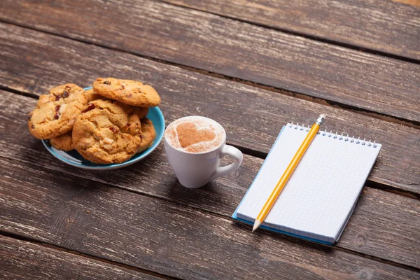 Cookie and cup with coffee, pencil and notebook. — Stock Photo, Image