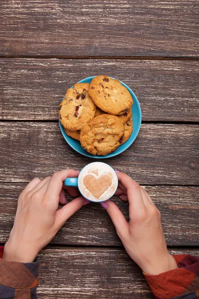 Female hands holding cup of coffee and cookies on wooden table. — Stock Photo, Image