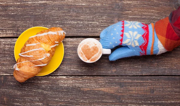 Mão feminina em luva segurando xícara de café perto de croissant no woo — Fotografia de Stock