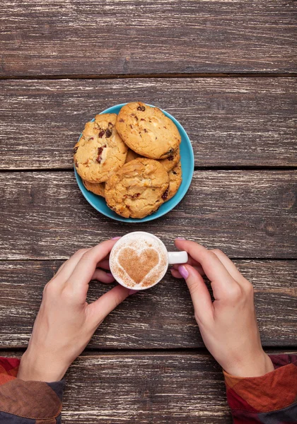 Kobiece ręce trzyma kawę i ciasteczka na drewnianym stole. — Zdjęcie stockowe