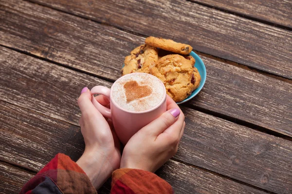 Frauenhände halten Tasse Kaffee und Kekse auf Holztisch. — Stockfoto